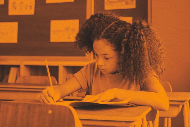 girl sitting in classroom writing in book with pencil